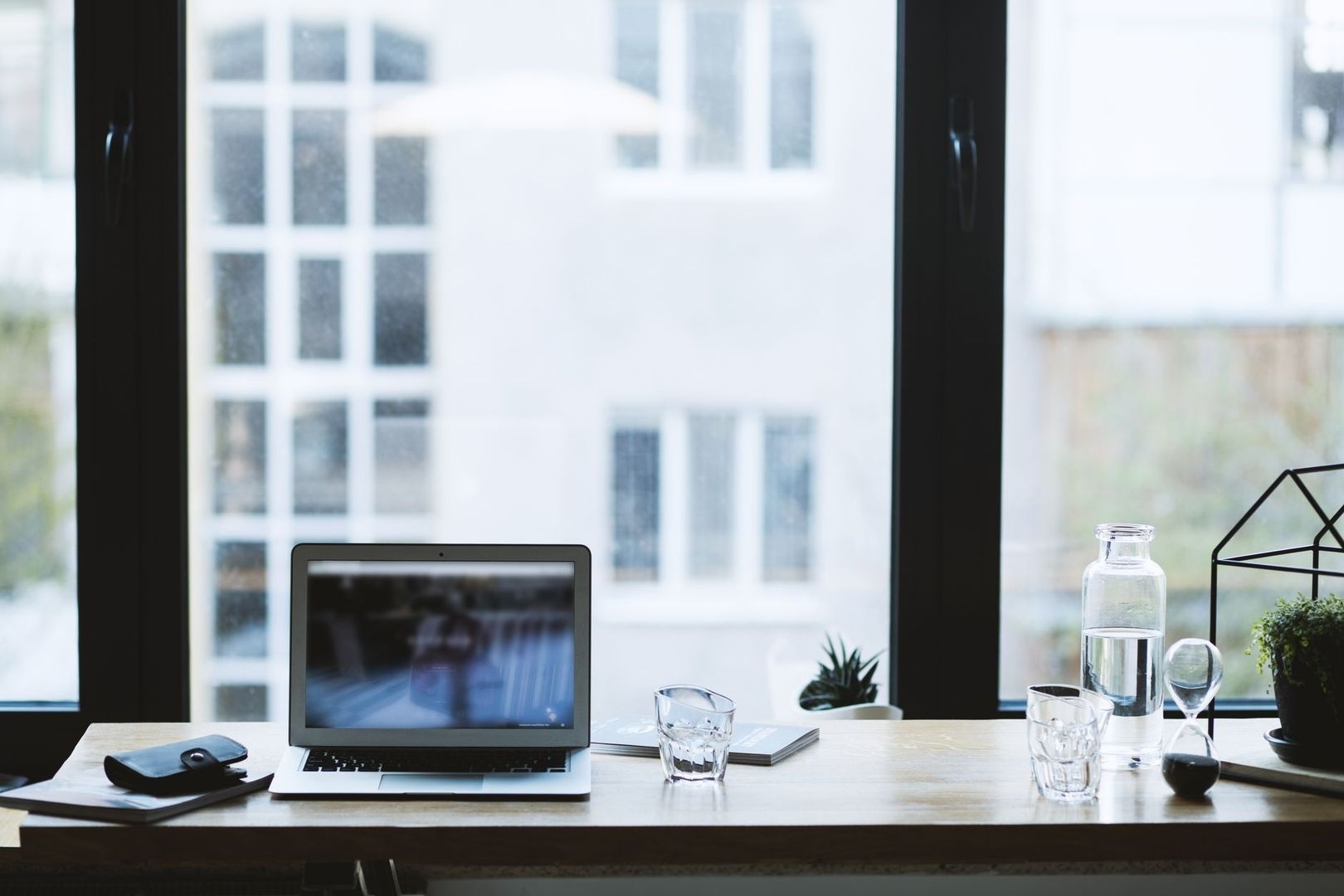 Minimalistiskt skrivbord med laptop, glas och växter vid ett stort fönster